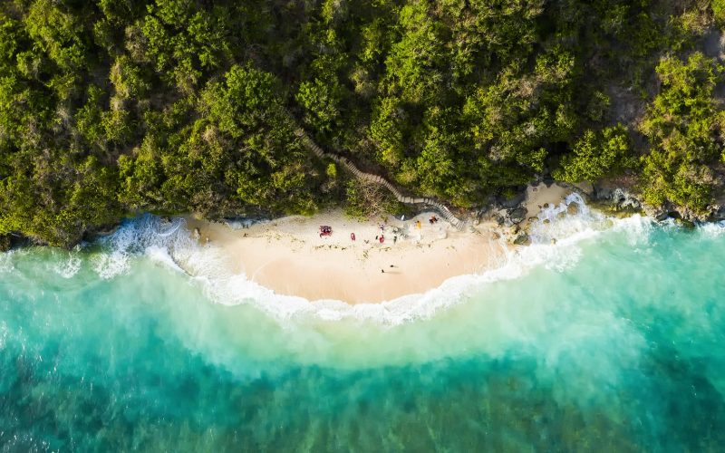 View from above, stunning aerial view of some tourists sunbathing on a beautiful beach bathed by a turquoise rough sea during sunset, Topan Beach, South Bali, Indonesia.